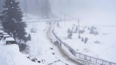 Tourists walk through a snow-covered road during the season's first snowfall at Gulmarg in Baramulla district of North Kashmir on Thursday. (PTI Photo)