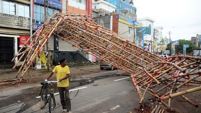 A man walks past a makeshift bamboo gate uprooted due to strong winds under the impact of Cyclone Sitrang, in Agartala on Tuesday. (ANI) A man walks past a makeshift bamboo gate uprooted due to strong winds under the impact of Cyclone Sitrang, in Agartala on Tuesday. (ANI)