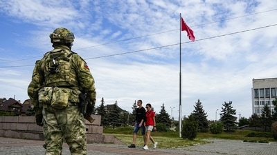 Russia-Ukraine War: A young couple walks past a Russian soldier guarding an area in Kherson. (AP)