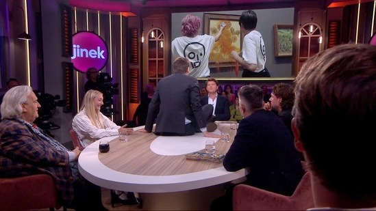 The video shows a man, initially seated as one of the panellists in the show called ‘Jinek’, taking the glue out of his pocket, climbing on the table and sticking himself on top.(Twitter/@Jelle_De_Graaf)