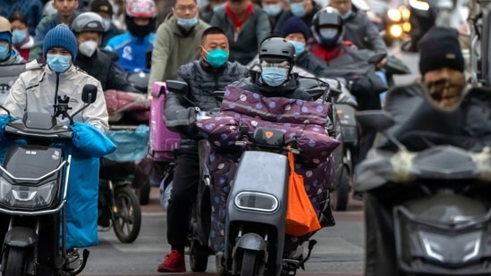 Covid In China: Commuters wearing face masks ride scooters along a street in the central business district in Beijing. (AP)