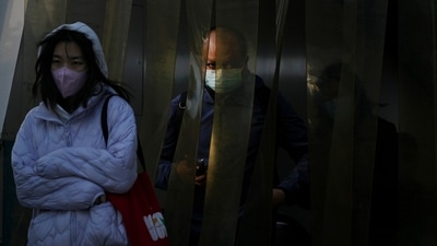 Covid In China: Commuters wearing face masks walk through the plastic curtain in Beijing. (AP) Covid In China: Commuters wearing face masks walk through the plastic curtain in Beijing. (AP)