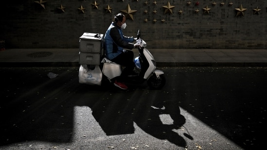 Covid In China: A food delivery rider wearing a face mask rides in Beijing.(AP)