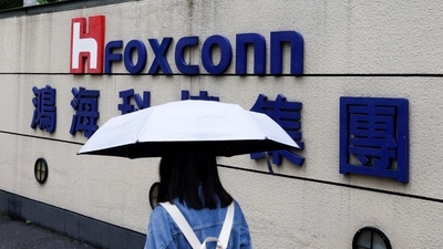 Covid In China: A woman carrying an umbrella walks past the logo of Foxconn. (Reuters)