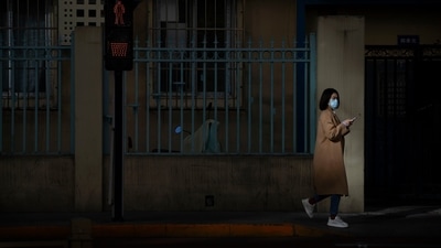 Covid In China: A woman wearing a face mask walks along a street in Beijing. (AP) Covid In China: A woman wearing a face mask walks along a street in Beijing. (AP)