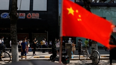 Covid In China: A China's flag flutters near people lining up to get tested at a makeshift nucleic acid testing site. (Reuters)
