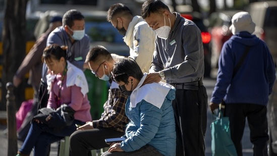 Covid In China: Workers wearing face masks give massages to customers as they sit on chairs on a sidewalk in Beijing.(AP)