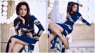 Ankita Lokhande's jade blue dress features an abstract print in silver and grey hues. It has a deep neckline accentuating her décolletage, full-length sleeves, wrapover detail on the bust with a bow tie, a maxi hem length, a risqué thigh-high slit, and a figure-hugging fitting highlighting Ankita's curves.  (Instagram)