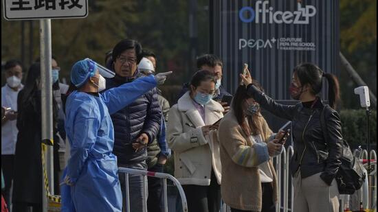 A woman (right) wearing a mask shows her health check QR code as she and others line up to get their routine Covid-19 throat swabs at a testing site in Beijing, on Tuesday. (AP)