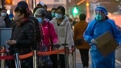 Covid In China: A worker wearing a protective suit walks past people waiting in line for COVID-19 tests. (AP) Covid In China: A worker wearing a protective suit walks past people waiting in line for COVID-19 tests. (AP)