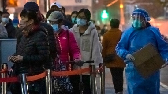 Covid In China: A worker wearing a protective suit walks past people waiting in line for COVID-19 tests. (AP)