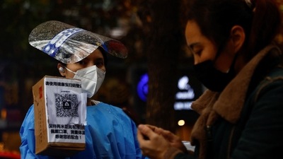 A worker in a protective suit guides people to scan health QR code at a nucleic acid test booth for the coronavirus disease in Beijing, China on November 11. (Reuters)