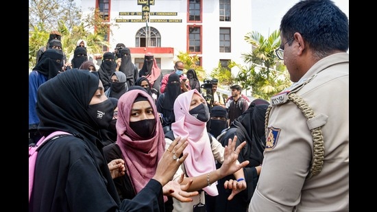 Female Muslim students wearing burqa and hijab talk to a police officer during their protest, outside the Shivamogga District collector's office, in Shivamogga, February 17, 2022 (PTI)