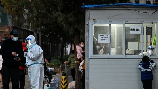 Covid In China: A health worker talks with a man while a health worker inside a nucleic acid testing station gets a swab sample.(AFP)