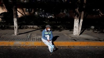 Covid In China: A pandemic prevention worker in a protective suit rests in the sun. (Reuters)