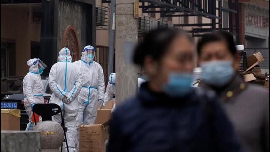 Residents walk near pandemic prevention workers in protective suits in a locked-down residential compound as outbreaks of the coronavirus disease (Covid-19) continue in Beijing, China (REUTERS)