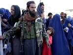 A Taliban fighter stands guard as people receive food rations distributed by a Saudi humanitarian aid group, in Kabul, Afghanistan, Monday, April.