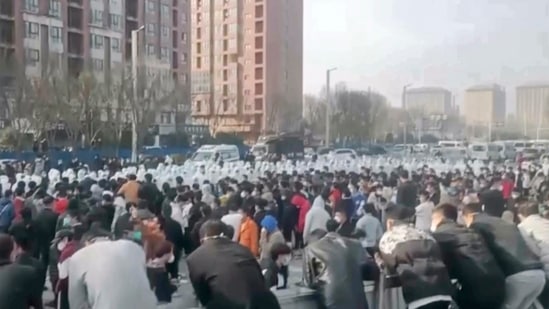 Protesters face off against security personnel in white protective clothing at the factory compound operated by Foxconn Technology Group who runs the world's biggest Apple iPhone factory in Zhengzhou in central China's Henan province. (AP)