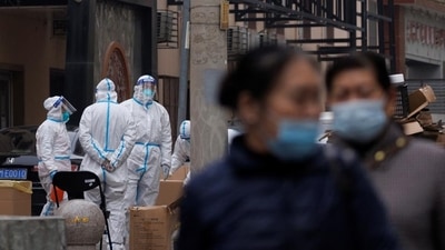 China: Residents walk near pandemic prevention workers in protective suits in a locked-down residential compound as outbreaks of the coronavirus disease (Covid-19) continue in Beijing. (Reuters) China: Residents walk near pandemic prevention workers in protective suits in a locked-down residential compound as outbreaks of the coronavirus disease (Covid-19) continue in Beijing. (Reuters)