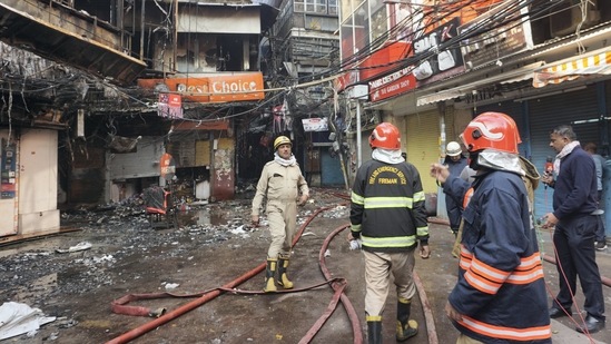 Fire Brigade personnel stand near burnt shops following a massive fire that broke out at the Bhagirath Palace market in Delhi.(PTI)