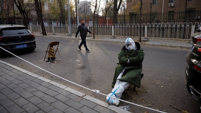 An epidemic prevention worker in a protective suit sleeps in a chair outside a locked-down residential compound as outbreaks of the coronavirus disease (COVID-19) continue in Beijing, China on Sunday. (Reuters) 