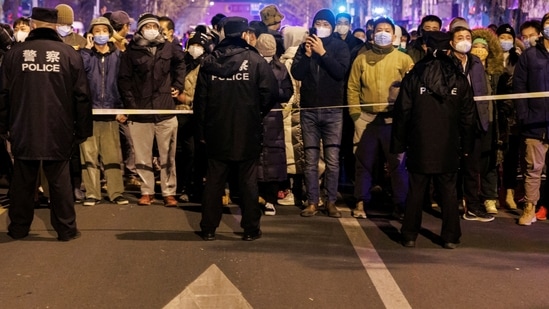 People stand behind a police cordon as they watch a protest over coronavirus disease (COVID-19) restrictions, following a commemoration of the victims of a fire in Urumqi, as outbreaks of COVID-19 continue, in Beijing, China, November 27, 2022. REUTERS/Thomas Peter