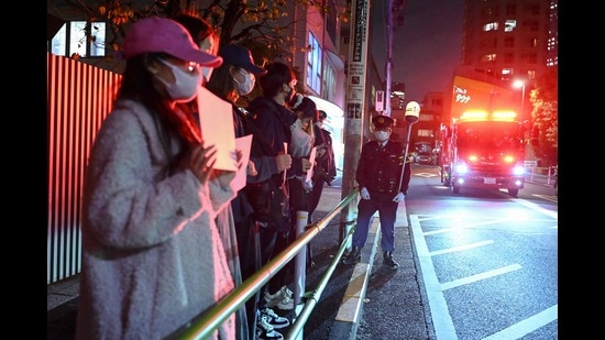 A fire truck (R) passes as a small group of protesters (L) hold up blank white pieces of paper in protest directly across the street from the Chinese embassy in Tokyo on November 28, 2022 (AFP)