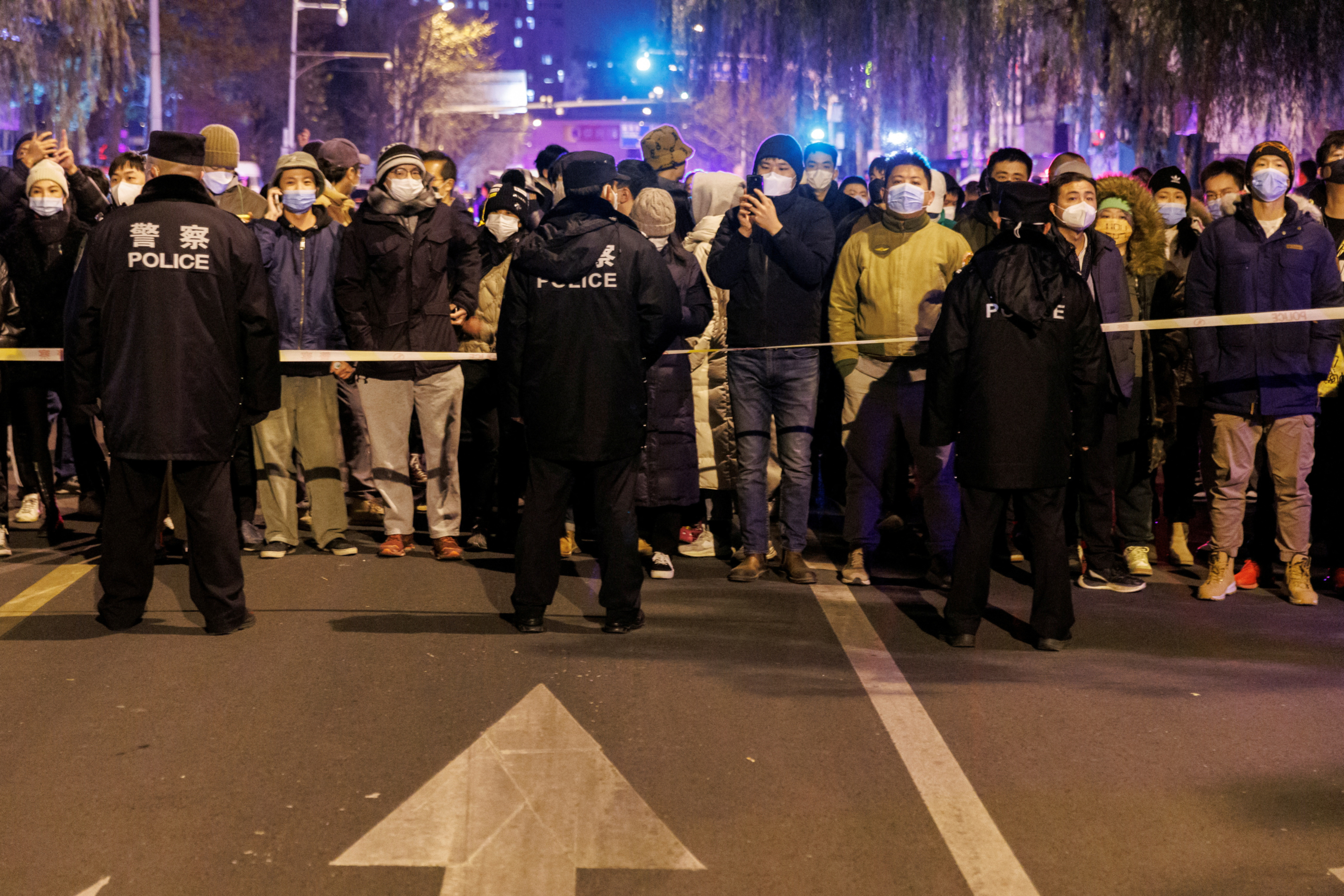 People stand behind a police cordon as they watch a protest over Covid restrictions, following a commemoration of the victims of a fire in Urumqi. (Reuters Photo)