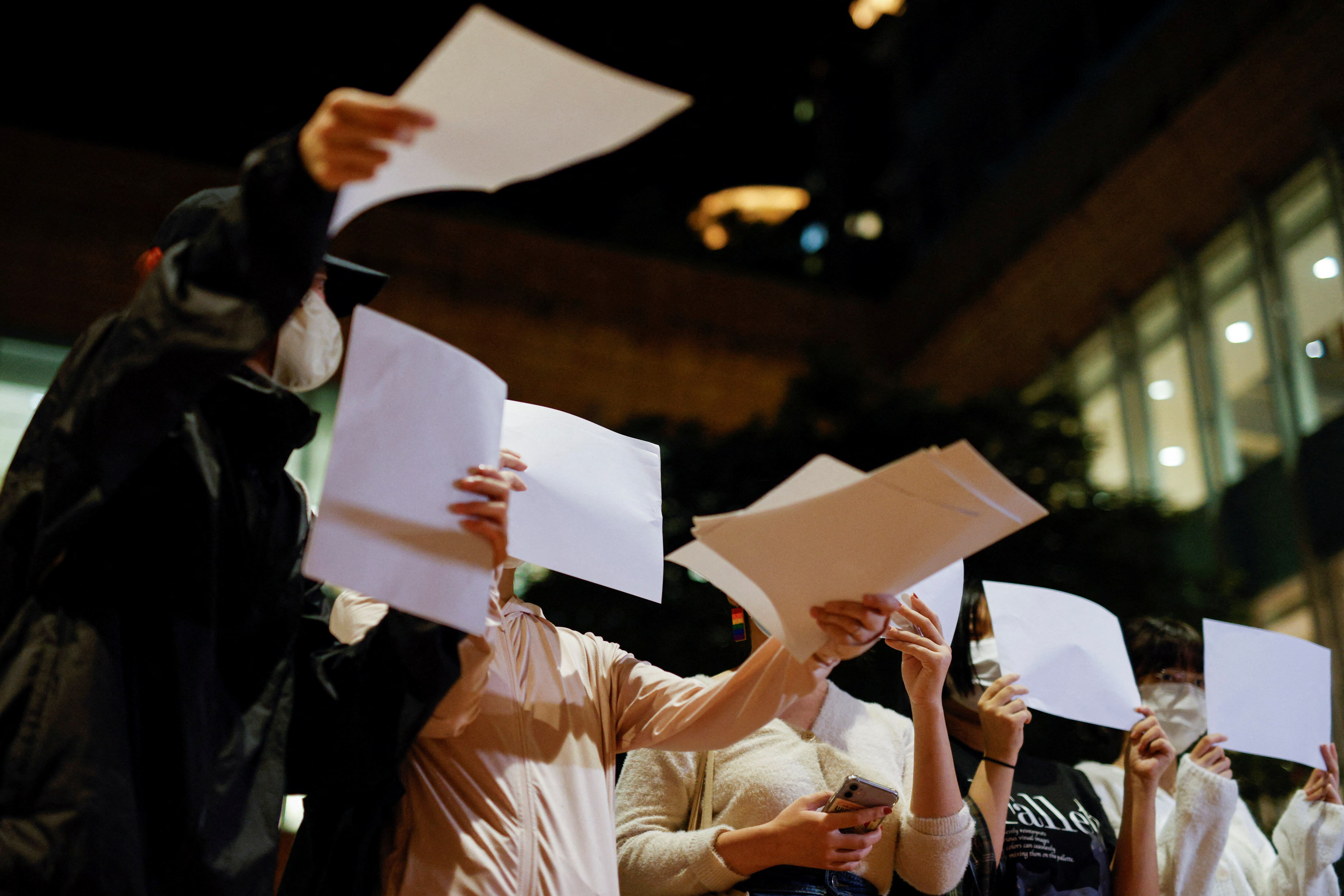 Women hand out sheets of paper in protest over coronavirus disease (Covid-19) restrictions in mainland China, during a commemoration of the victims of a fire in Urumqi, at the University of Hong Kong (HKU), in Hong Kong, China November 29, 2022. (REUTERS/Tyrone Siu)