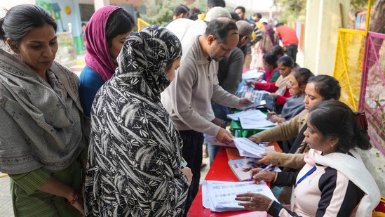 Polling agents look for the names of the people in a list as they come to cast their votes for the MCD elections, at a polling station in Khureji Khas, in East Delhi, Sunday, December 4, 2022. (PTI Photo/Manvender Vashist Lav)