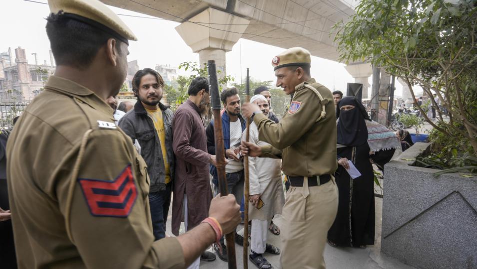 Police personnel stand guard as voters wait to cast their votes for the Municipal Corporation of Delhi (MCD) elections, at a polling station in Jafrabad in north-east Delhi on Sunday. (PTI)