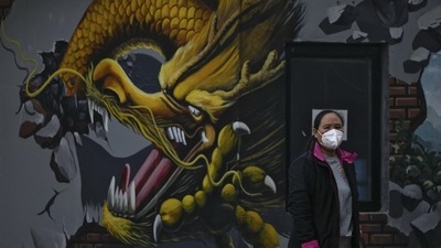 Covid In China: A woman wearing a face mask stands near a mural depicting a dragon in Beijing. (AP)