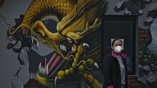 Covid In China: A woman wearing a face mask stands near a mural depicting a dragon in Beijing. (AP)