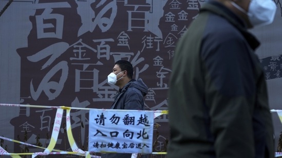 Residents wearing face masks walk past caution tapes as they head for their routine Covid-19 throat swabs collection at a testing site in Beijing, on December 6. China may announce 10 new nationwide easing measures as early as December 7, two sources with knowledge of the matter told Reuters.(Andy Wong / AP)