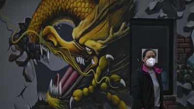 Coronavirus: A woman wearing a face mask stands near a mural depicting a dragon in Beijing. (AP) Coronavirus: A woman wearing a face mask stands near a mural depicting a dragon in Beijing. (AP)