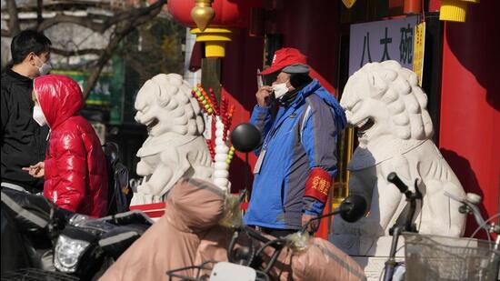 A pandemic volunteer adjusts his mask near stone lions outside a supermarket in Beijing, on Wednesday. In a sharp reversal, China has announced a series of measures rolling back some of the most draconian anti-Covid-19 restrictions. (AP)