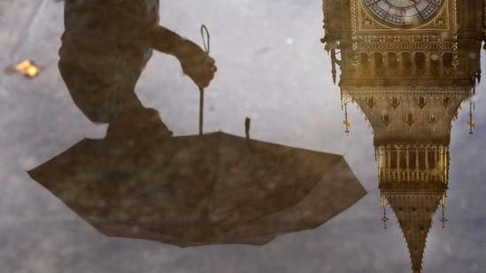 Britain Power Cuts: A woman with an umbrella and the Elizabeth Tower also known as Big Ben are reflected in a puddle in London.(AP)