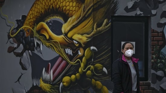Coronavirus: A woman wearing a face mask stands near a mural depicting a dragon in Beijing.(AP)
