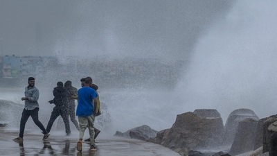 People stand near a stone ledge amid gusty winds as dark clouds loom over the Kasimedu fishing harbour in Chennai on Thursday. (AFP) People stand near a stone ledge amid gusty winds as dark clouds loom over the Kasimedu fishing harbour in Chennai on Thursday. (AFP)