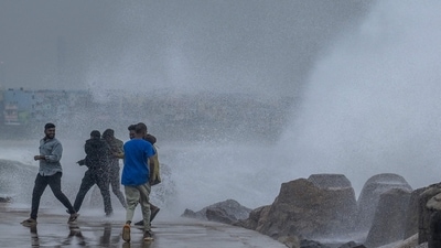 Cyclone Mandous: People stand near a stone ledge amid gusty winds as dark clouds loom over the Kasimedu fishing harbour in Chennai on December 8, 2022. (AFP) Cyclone Mandous: People stand near a stone ledge amid gusty winds as dark clouds loom over the Kasimedu fishing harbour in Chennai on December 8, 2022. (AFP)