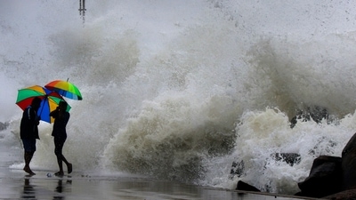 People hold their umbrella as they walk on an embankment against gusty winds and high waves in Chennai. (AP Photo)