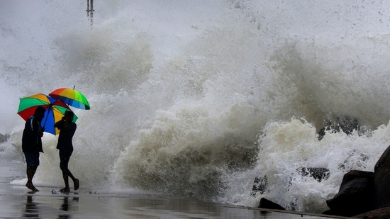 People hold their umbrella as they walk on an embankment against gusty winds and high waves in Chennai.(AP Photo)