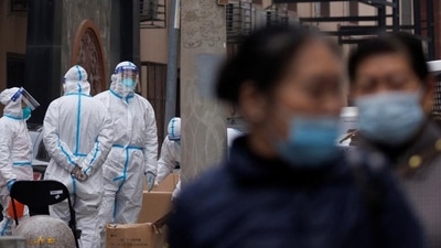 Covid In China: Residents walk near pandemic prevention workers in protective suits in a locked-down residential compound as outbreaks of the coronavirus disease (Covid-19) continue in Beijing. (Reuters) Covid In China: Residents walk near pandemic prevention workers in protective suits in a locked-down residential compound as outbreaks of the coronavirus disease (Covid-19) continue in Beijing. (Reuters)