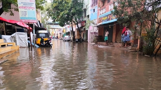 People stand on the waterlogged path after it got flooded due to heavy rainfall triggered by Cyclone Mandous, at MMDA Colony, Arumbakkam, in Chennai on Saturday.(ANI)