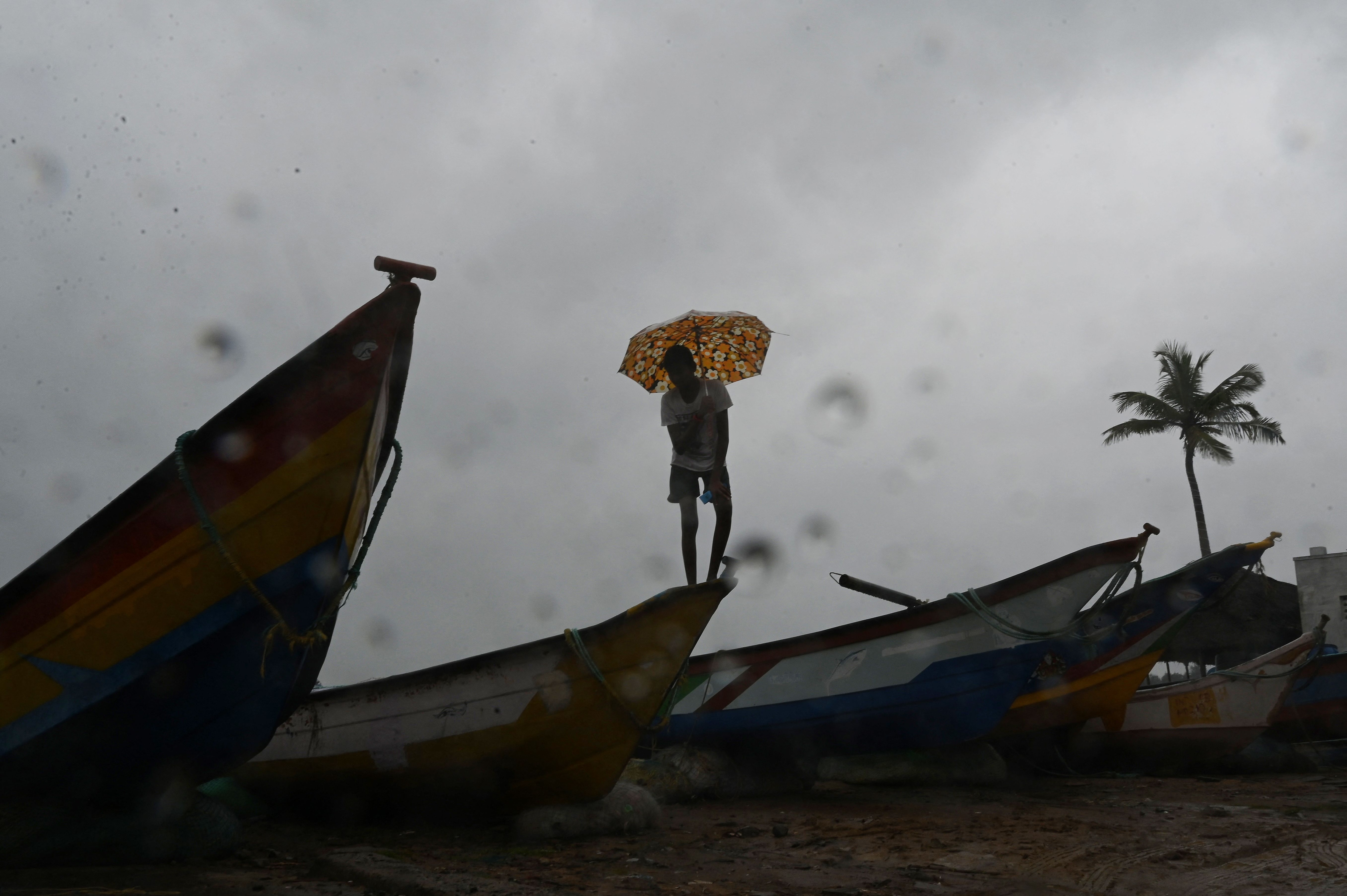 Cyclone Mandous: A man with an umbrella stands over fishing boats stationed along a beach in Mahabalipuram. (AFP)