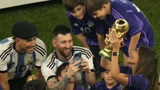 Argentina's Lionel Messi takes pictures of his wife Antonela Roccuzzo as she holds the winners trophy after Argentina won the FIFA World Cup final soccer match against France at the Lusail Stadium.(AP)