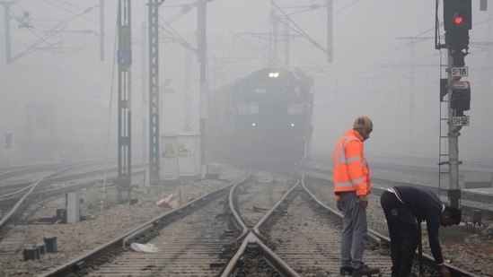 Workers repair a railway track as a train approaches amid low visibility in Amritsar, on December 20. Several trains in Delhi were reported to be running late by a few hours on December 21 due to poor visibility induced by fog. Flight operations remained unaffected, HT reported.(PTI )