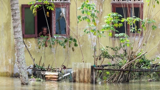A man speaks on his phone from inside a house partially submerged by floodwaters in Pasir Mas, Kelantan, on December 21. According to AFP, four people died in the area on December 19 when three sisters were electrocuted while wading in the floodwaters and a 15-month-old boy drowned.(AFP)