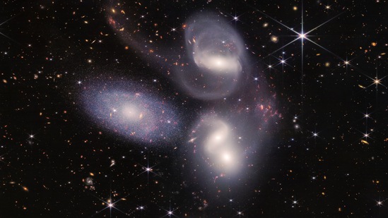Sparkling clusters of millions of young stars and starburst regions of fresh star birth grace the image. Sweeping tails of gas, dust and stars are being pulled from several of the galaxies due to gravitational interactions. (NASA, ESA, CSA, STScI)