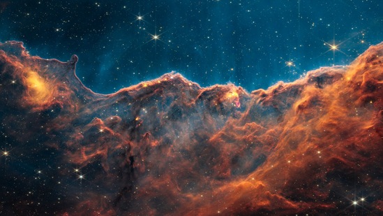 The ‘Cosmic Cliffs’ of the Carina Nebula is captured in an image divided horizontally by an undulating line between a cloudscape forming a nebula along the bottom portion and a relatively clear upper portion.(NASA, ESA, CSA, STScI)